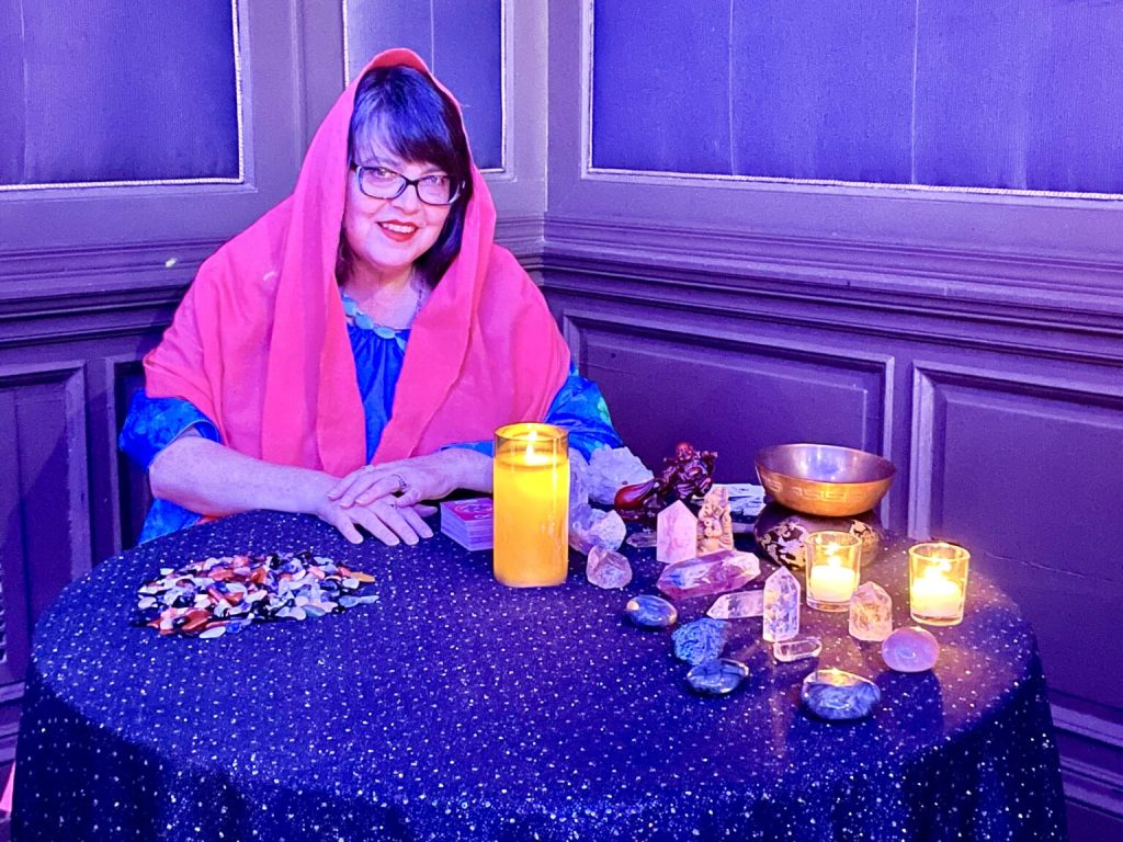 Izolda wears pink shawl at a table with crystals, candles and tarot cards