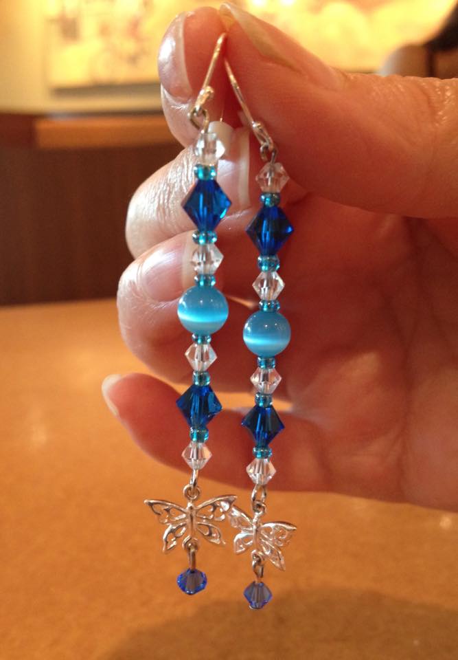 hand holding long blue earrings with butterflies on the end